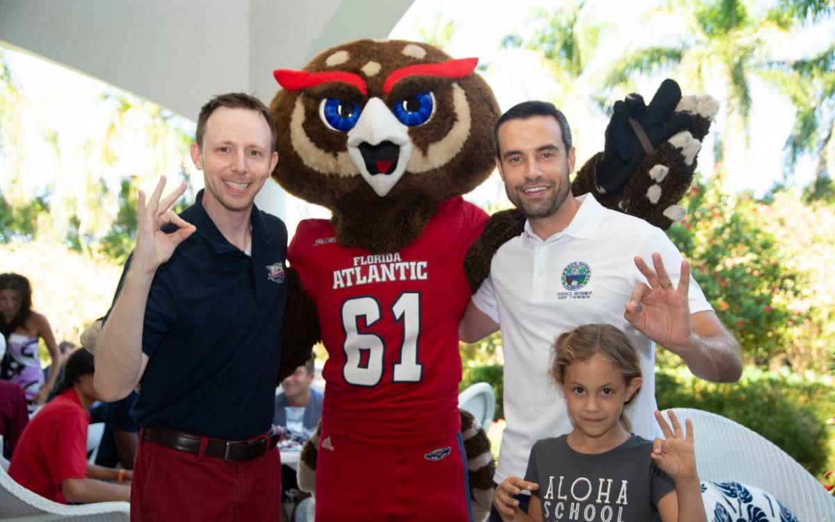 People posing and smiling with Owlsley mascot, holding up Owl Fingers