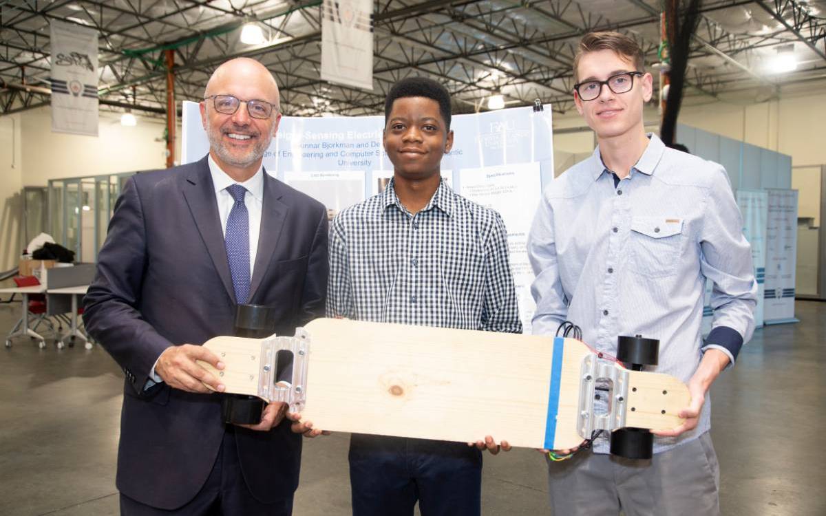 Two students and professor posing with motorized skateboard