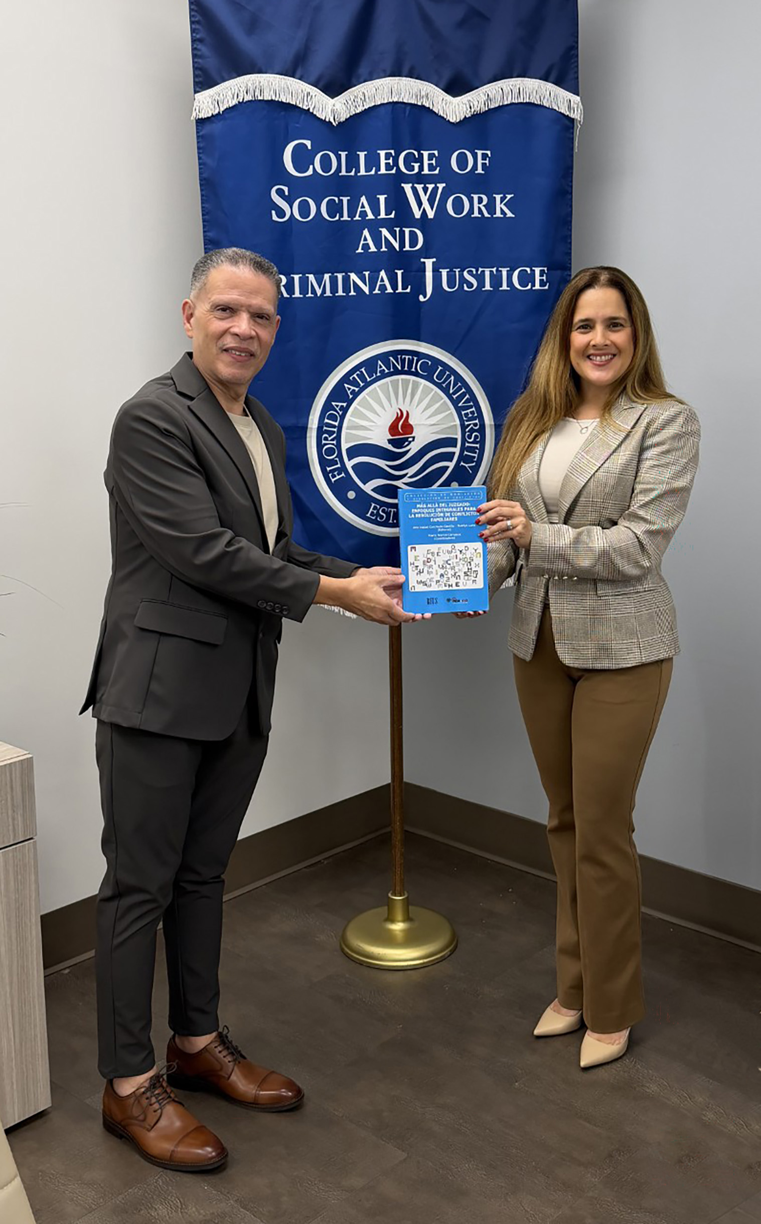 Dr. Manny John González and Dr. Naelys Luna hold a copy of the book in front of a College of Social Work and Criminal Justice banner.