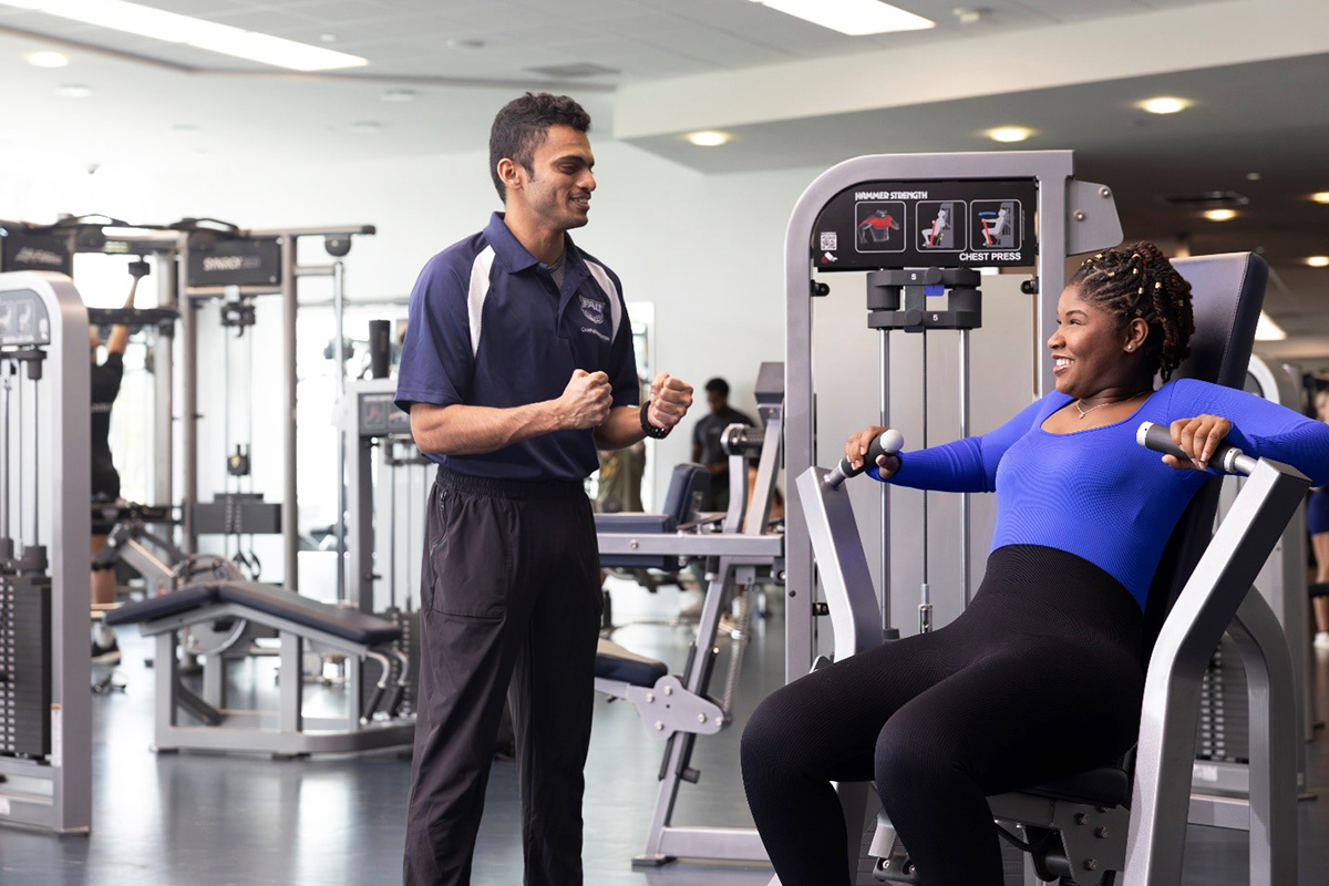 A personal trainer with a student on a machine