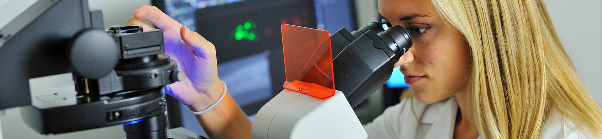 Female wearing lab coat looking into microscope