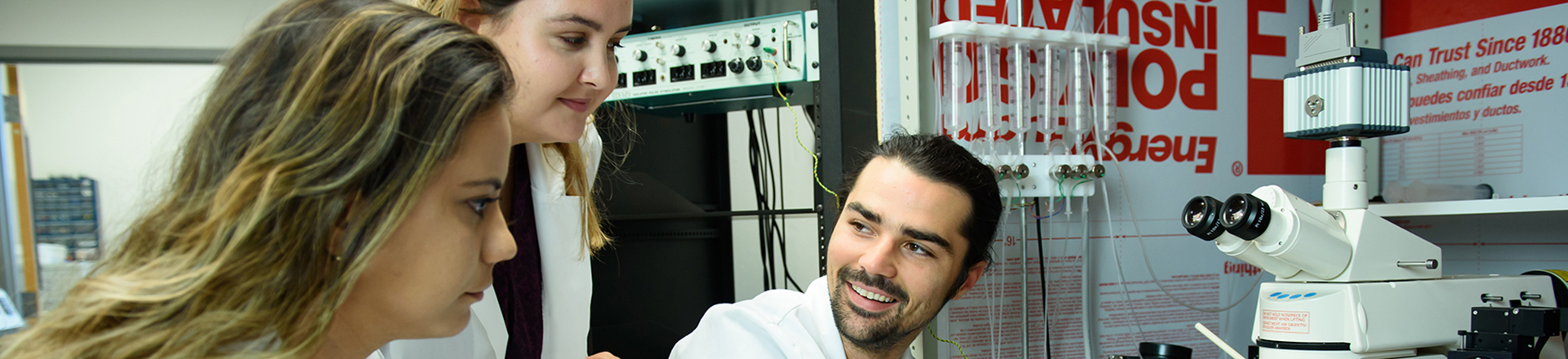 Male and two female students in lab coats looking at lab equipment in a lab