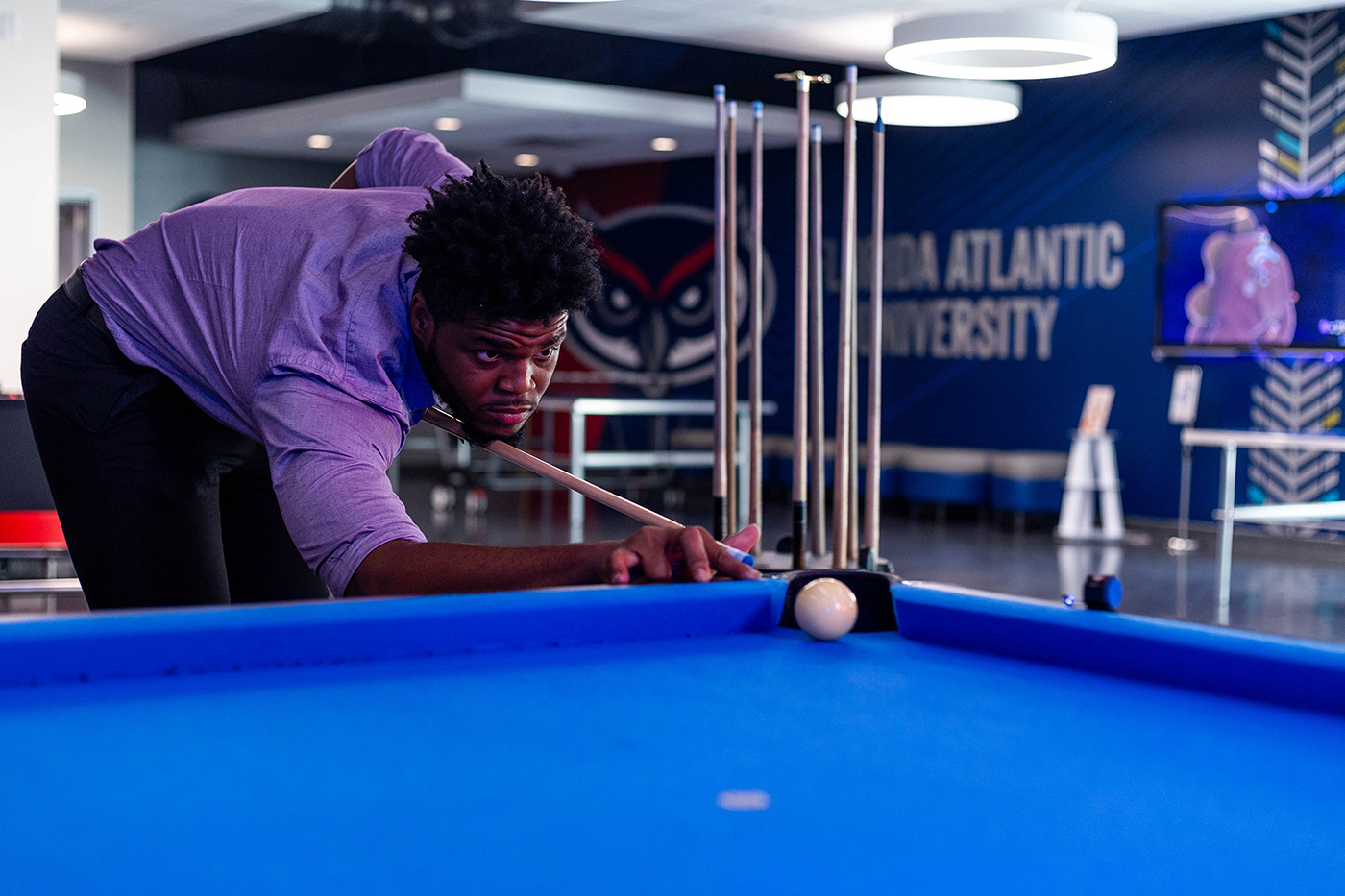 a man leaning forward with a pool cue in hand, intently focused on a game of pool/billiards