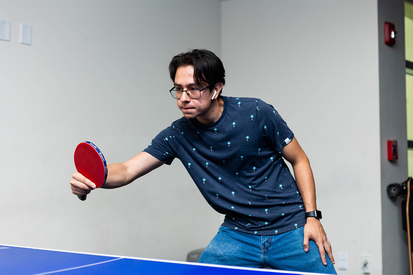 a young man focused on a game of ping pong, red paddle in hand